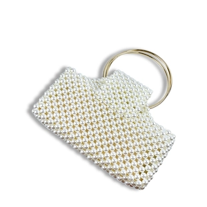 Detailed close-up of woven pearl beads and golden metal ring handles on an evening bag