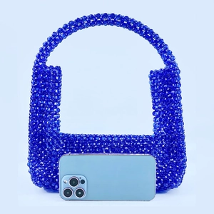 Detailaufnahme der blauen Perlenhandtasche mit Rundgriff neben einem Smartphone