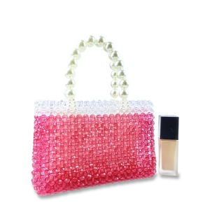Detailed view of handmade pink beaded handbag with large faux pearl handle on white background