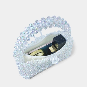 Détail d'un sac à main en perles irisées avec pochette blanche et accessoires de maquillage