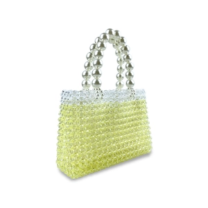 Detailed view of yellow beaded handbag featuring a white pearl handle and woven grid texture