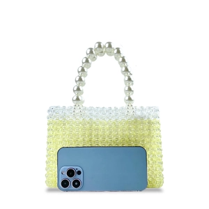 Macro detail of yellow beaded mini bag with pearl handle next to a smartphone