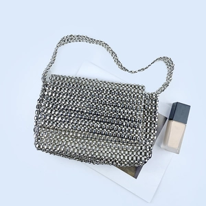 Detail of silver beaded flap bag showing woven texture on a minimalist book background