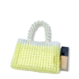 Detail of yellow beaded handbag with pearl handle shown next to a foundation bottle