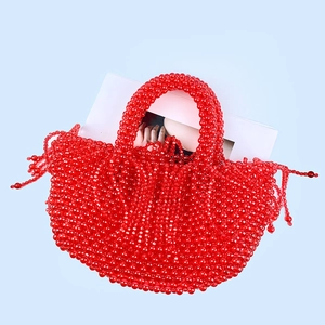 Détail du sac à main rouge en perles artisanales avec pompons sur un fond bleu clair