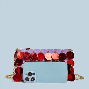 Detail of purple sequin mini bag with gold chain strap shown next to a smartphone