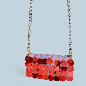Close-up of overlapping red metallic sequins and gold chain strap on purple handbag