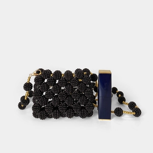 Detailed macro shot of a black and gold handmade beaded mini bag next to a lipstick scale
