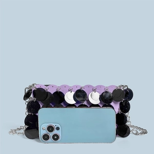 Detailed view of a purple sequin clutch with silver chain next to a smartphone