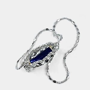 Close-up of woven silver mesh pendant featuring a deep blue stone with golden accents
