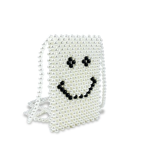 Detail view of handmade white pearl woven crossbody bag with black smiley face pattern