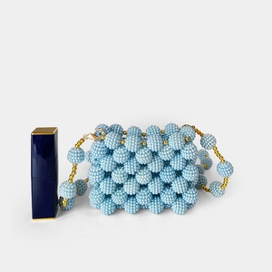 Close-up of light blue handmade beaded mini bag with gold chain next to a lipstick