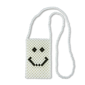 Detail of handmade white pearl woven crossbody bag featuring a black beaded smiley face