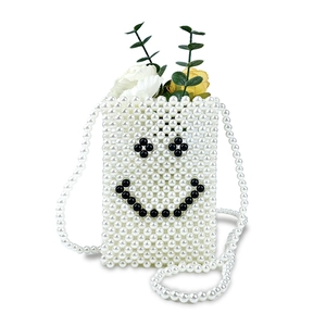 Detailed view of handmade pearl crossbody bag featuring a woven black pearl smiley face