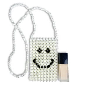 Detail of handmade woven pearl bag with black smiley face pattern and slim shoulder strap