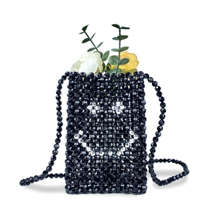 Detail of handmade black beaded crossbody mini bag with a white pearl smiley face pattern
