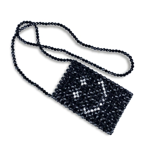 Detail of handmade black beaded crossbody bag featuring a white beaded smiley face pattern