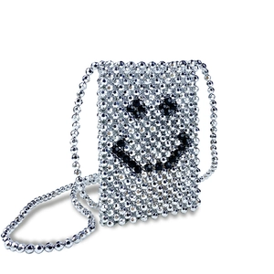 Detail of silver beaded crossbody bag featuring a woven black beaded smiley face pattern