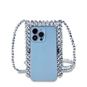 Macro shot of silver beaded crossbody bag holding a blue smartphone with shiny texture