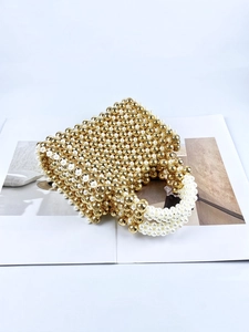 Handmade beaded handbag with gold and pearl beads on a magazine in 45-degree view
