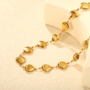 Collier doré à breloques coquillages sur un support géométrique blanc minimaliste