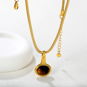 Collier chaîne serpent dorée avec pendentif œil de tigre sur un fond minimaliste