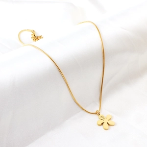 Détail du pendentif fleur dorée sur chaîne serpent posé sur un tissu de soie blanc