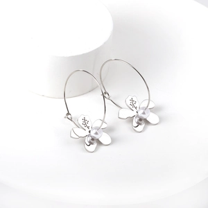 Boucles d'oreilles créoles fleurs argentées avec perles sur un présentoir épuré