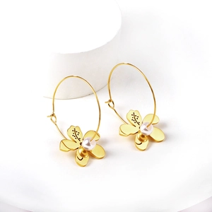 Détail macro de boucles d'oreilles fleurs dorées avec perles blanches et plaquage 18K