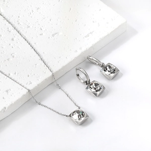 Détail macro d'un ensemble pendentif en cristal carré et boucles sur pierre blanche