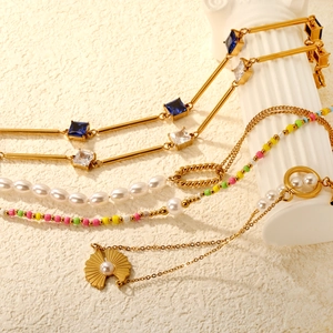 Dettaglio di un bracciale dorato con perle a cuore e zirconi blu su colonna bianca