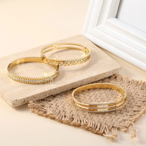 Three 18K gold plated stainless steel bracelets with rhinestones on a stone and linen base
