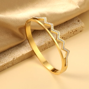 Close-up of golden wavy double-layer bangle with sparkling pavé crystals on stone texture