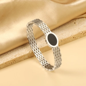 Detail of hollow geometric mesh bracelet with black oval inlay on beige stone stand