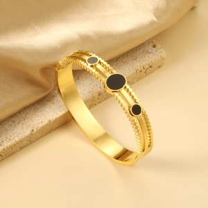 Detail of 18K gold plated bangle featuring black round inlays and double bead edging