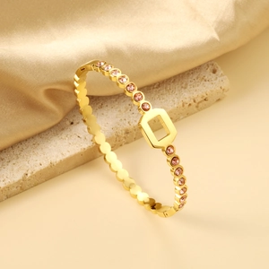 Detail of 18K gold-plated bangle with pink gemstones and wavy gear edges on silk
