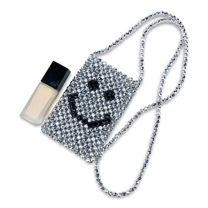 Detail of silver beaded mini crossbody bag featuring a black smiley face pattern