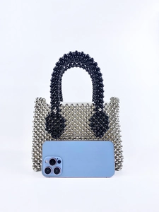 Silver beaded handbag detail with black handle and smartphone for scale reference