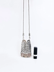 Mini sac bandoulière à paillettes argentées avec chaîne en métal à côté d'un rouge à lèvres
