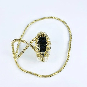 Macro shot of handcrafted gold beaded necklace with a central black obsidian gemstone