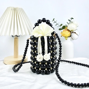 Detail view of a black beaded bucket bag featuring a white silk drawstring and gold accents
