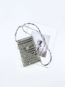 Artistic layout of a silver beaded crossbody phone bag with chain strap on white surface