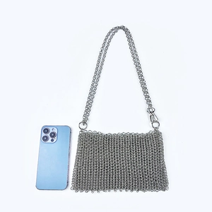 Detail of silver chainmail bag with metallic sequins and crossbody strap next to a phone