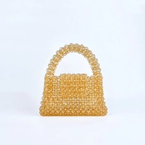 Détail du sac à main perlé ambre avec poignée courbée et design tissé à rabat