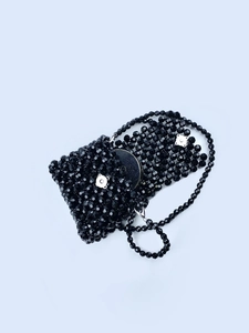 Close-up of black beaded handbag featuring magnetic silver clasps and woven pearl texture