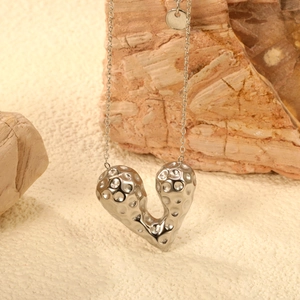 Macro detail of silver heart necklace with hammered texture on natural stone surface