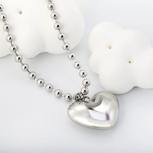 Detail of silver heart pendant with mirror finish and ball chain on white decor