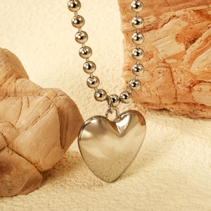 Detailed shot of polished silver heart pendant on ball chain with textured stone background