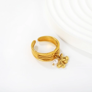 Detail of adjustable gold ring with hanging pearl and heart charms on a ceramic tray