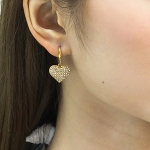 Détail de boucles d'oreilles cœur en or avec cristaux portées par un mannequin en gros plan